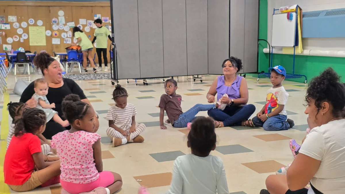 Caregivers, toddlers and a baby sitting in a circle on the floor during a Dance With Me class