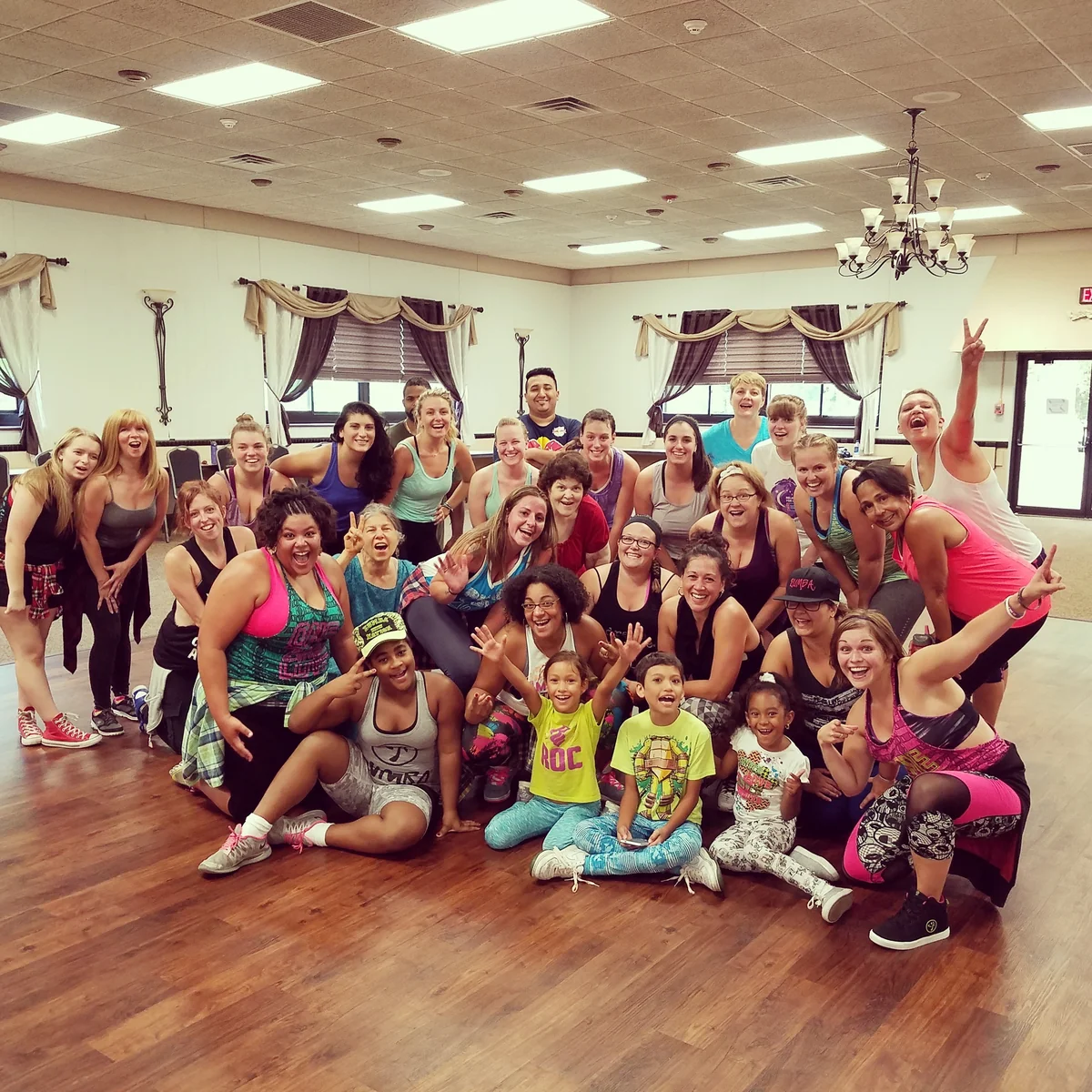 Large group of adults and children smiling together after a family-friendly Zumba class
